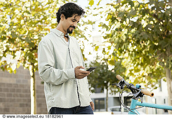 Smiling man using smart phone standing near bicycle