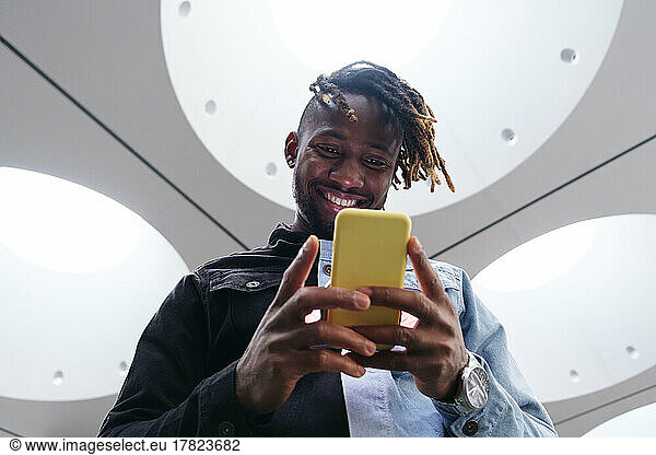 Smiling man using smart phone under illuminated ceiling