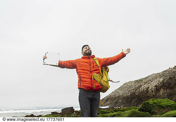 Smiling man wearing backpack standing with arms outstretched