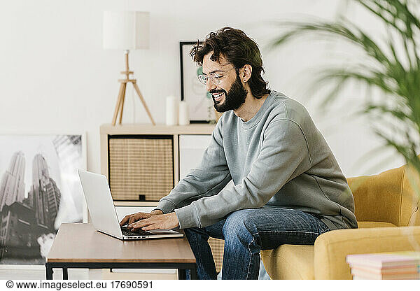 Smiling man wearing eyeglasses using laptop at home