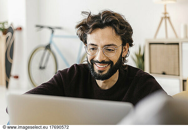 Smiling man wearing eyeglasses using laptop in living room at home