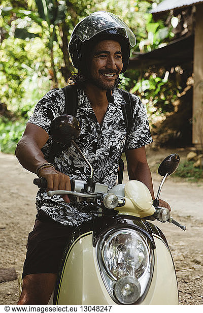 Smiling man wearing helmet while driving motor scooter on dirt road
