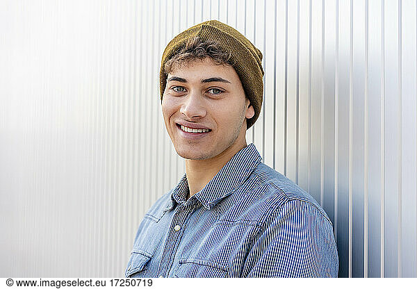 Smiling man wearing knit hat by silver colored wall
