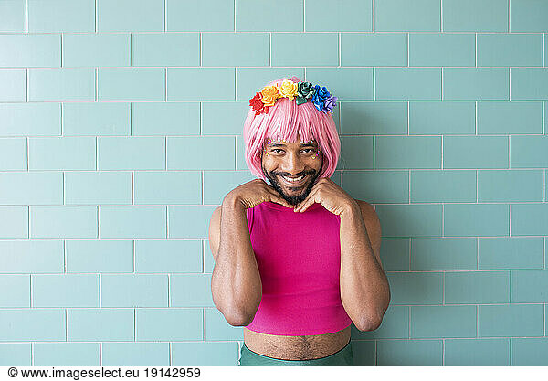 Smiling man wearing pink wig standing in front of wall