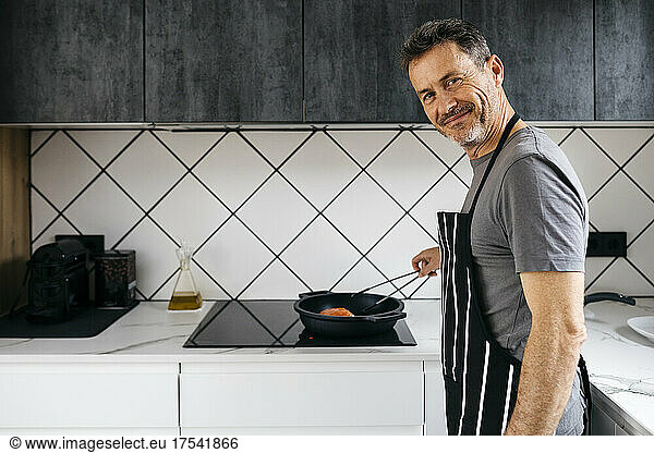 Smiling man with apron preparing food in kitchen at home