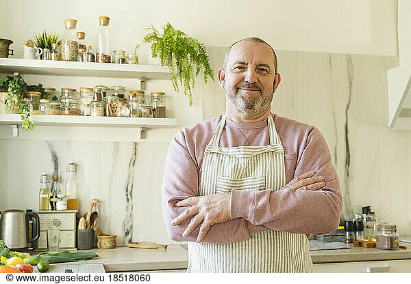 Smiling man with arms crossed standing in kitchen at home