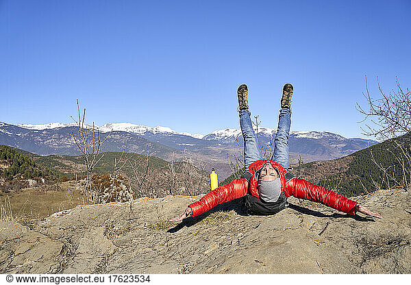 Smiling man with arms outstretched and legs up lying on rock