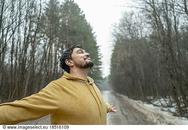 Smiling man with arms outstretched enjoying nature in rainy day