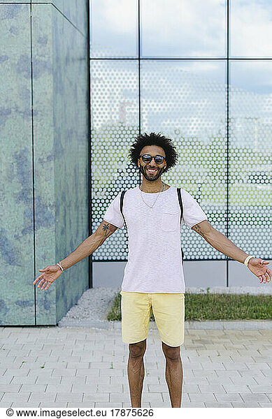 Smiling man with arms outstretched standing in front of glass building