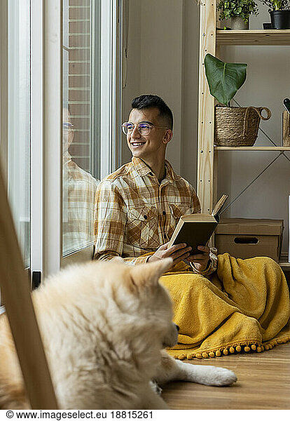 Smiling man with book looking out of window at home