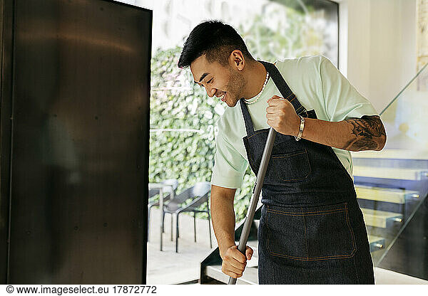 Smiling man with broom cleaning in coffee shop
