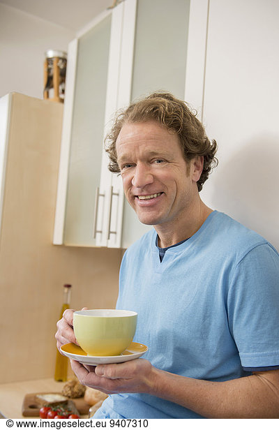 Smiling man with cup of coffee in kitchen