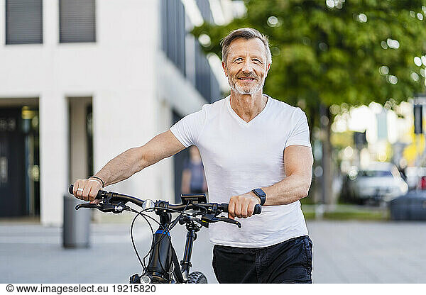 Smiling man with electric bicycle on footpath