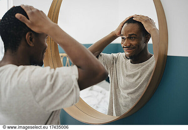 Smiling man with hand in hair looking in mirror at home