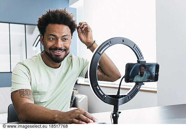 Smiling man with hand in hair making tutorial through smart phone at home