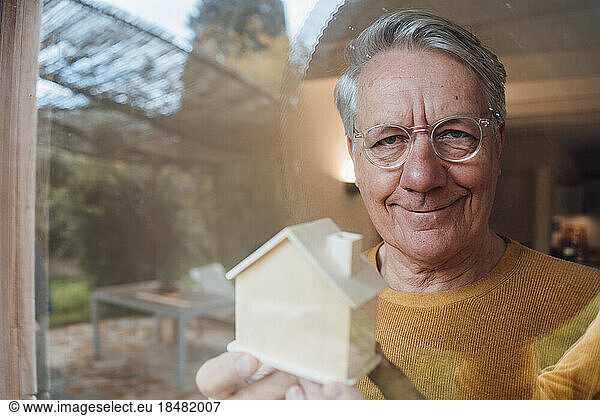 Smiling man with model house seen through glass