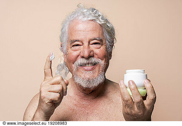 Smiling man with moisturizer on finger against beige background