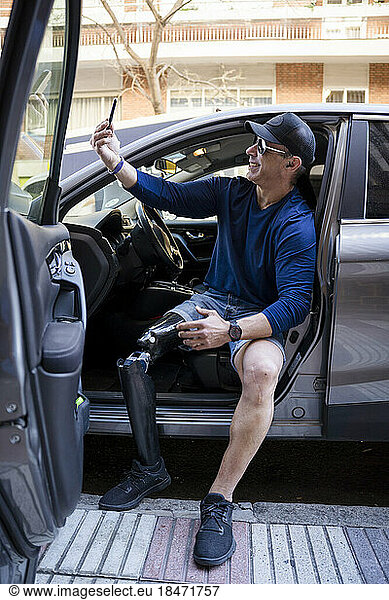 Smiling man with prosthetic leg taking selfie through smart phone sitting in car
