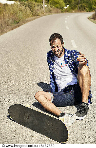 Smiling man with skateboard sitting on road