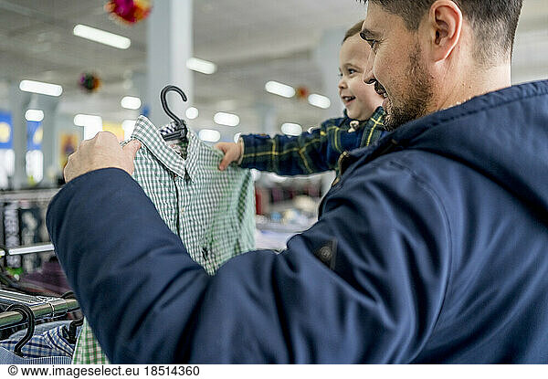 Smiling man with son choosing clothes in store