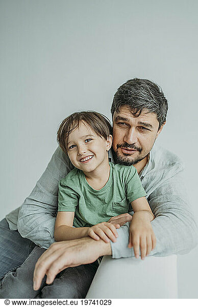 Smiling man with son sitting on sofa against white background