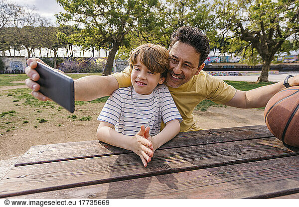 Smiling man with son taking selfie through smart phone sitting at table