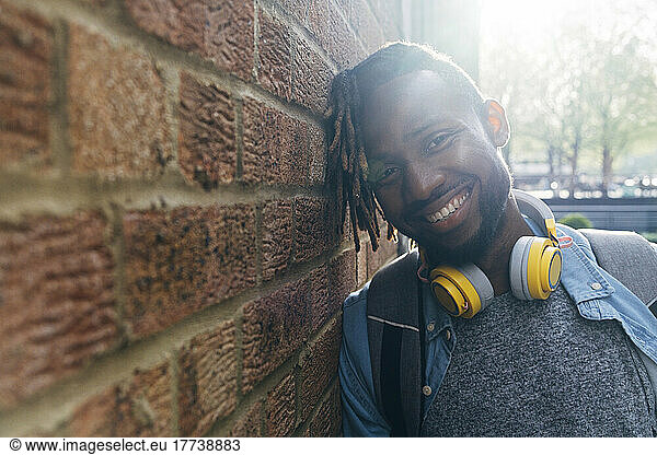 Smiling man with wireless headphones leaning on wall