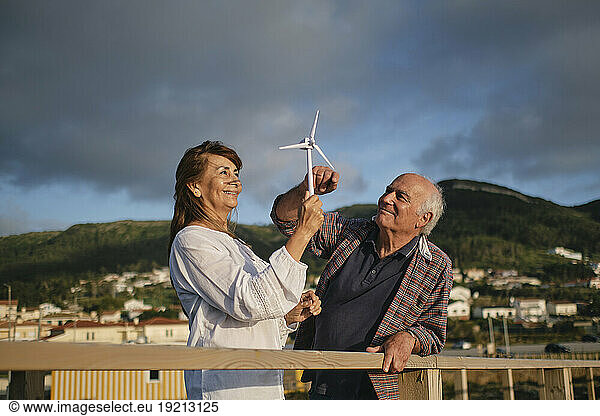 Smiling man with woman holding wind turbine under cloudy sky