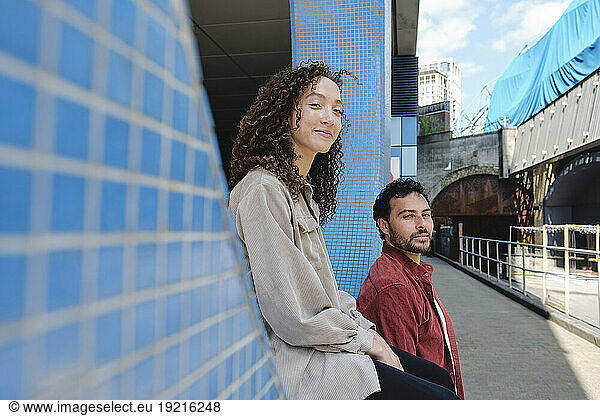 Smiling man with woman sitting on wall at footpath