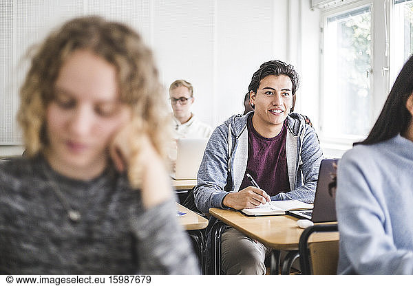 Smiling man writing in book at desk in classroom