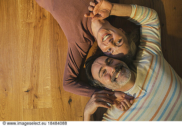 Smiling married couple lying on hardwood floor at home