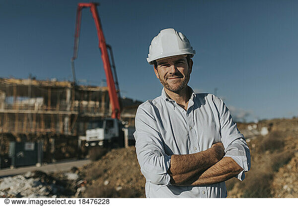 Smiling mature architect wearing hardhat standing at construction site