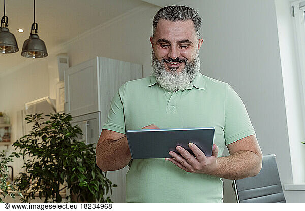 Smiling mature bearded man using tablet PC at home