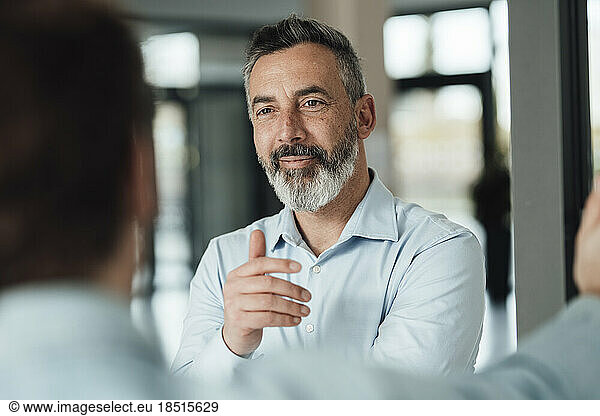 Smiling mature businessman gesturing and talking with colleague in office