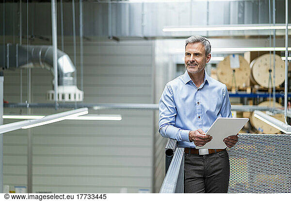 Smiling mature businessman holding digital tablet in factory