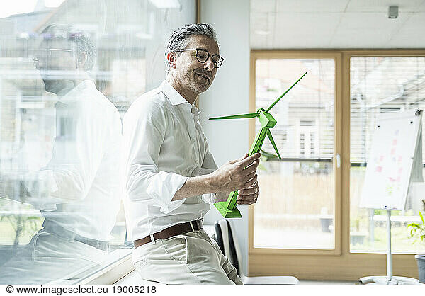 Smiling mature businessman looking at wind turbine model in office