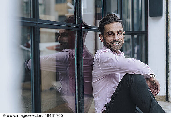 Smiling mature businessman sitting by glass door