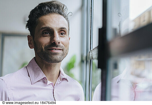 Smiling mature businessman standing by glass door