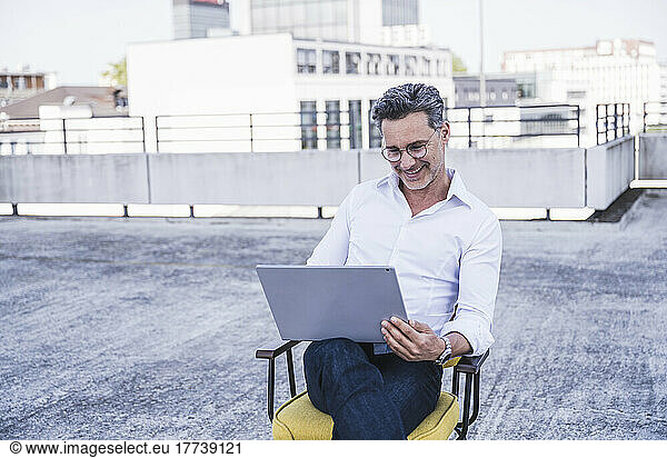 Smiling mature businessman using laptop sitting on chair