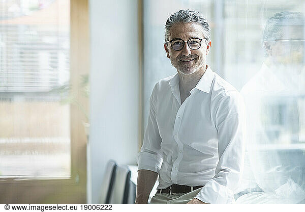 Smiling mature businessman wearing eyeglasses by window at office