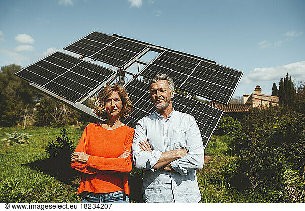 Smiling mature couple in front of solar panels on sunny day