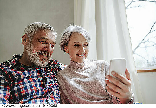 Smiling mature couple on video call over smart phone at home