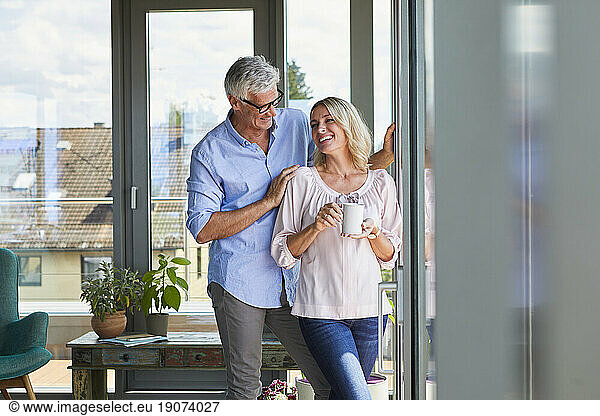 Smiling mature couple relaxing at home at the window