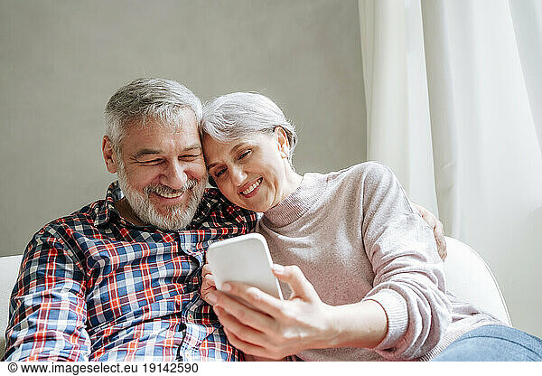 Smiling mature couple using smart phone sitting at home