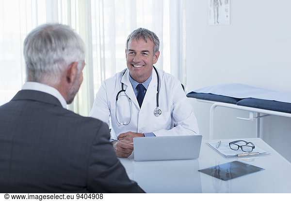 Smiling mature doctor and man sitting at desk in office
