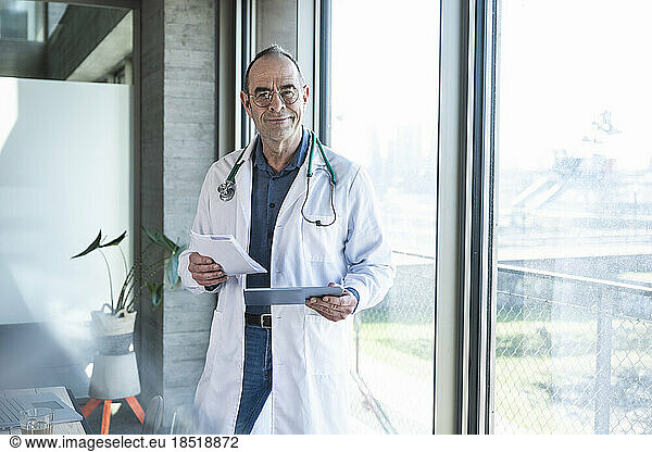 Smiling mature doctor holding prescription and tablet PC