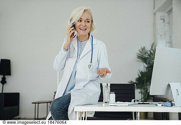 Smiling mature doctor talking on smart phone in clinic
