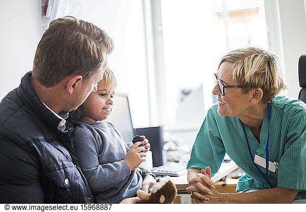 Smiling mature doctor talking to boy with father in clinic
