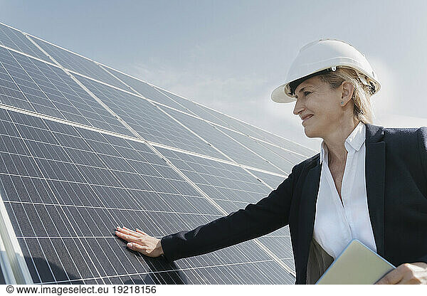 Smiling mature engineer touching and examining solar panels on sunny day