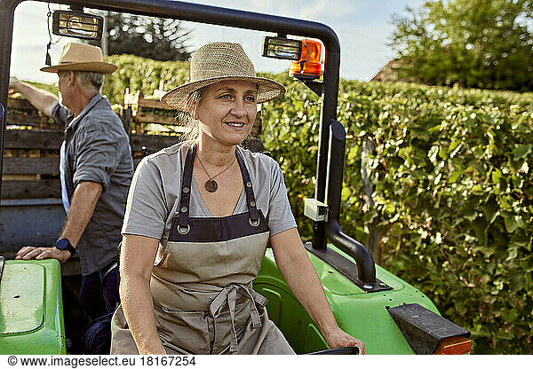 Smiling mature farmer driving tractor in front of colleague in vineyard